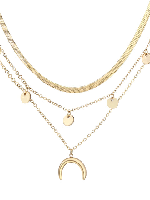 Four-layer gold necklace with herringbone chain, disc charms, and crescent moon pendant on cream background
