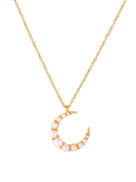 Gold crescent moon pendant with graduated white pearls on delicate chain against cream background